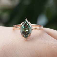 a woman's hand holding an engagement ring with a green tourmaline stone