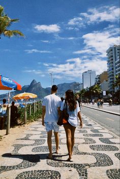 a man and woman walking down the sidewalk in front of some umbrellas on a sunny day