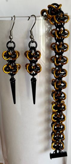 This chainmaille jewelry set consists of a bracelet and matching earrings in Halloween colors of black and orange. The jewelry is woven with connecting small anodized aluminum black rings with orange rings capturing a large black at the center.  The bracelet measures 8.5 inches in length which will fit a wrist that is between 7.5 to 7.75 inches comfortably. The black side locking tube clasp is enameled coated and will hold the bracelet securely. The earrings measure 2 inches in length from the stainless steel wires from which they hang. The earrings have 2 of the orbital links and have an enameled spike dangling from the links. They are very light to wear. Custom orders accepted on this set if you don't happen to like Halloween colors. Adjustable Black Chainmail Jewelry, Orange Rings, Chainmaille Jewelry Patterns, Chainmail Necklace, Chainmaille Jewelry, Halloween Colors, Bee Bracelets, Orange Ring, Chainmail Jewelry