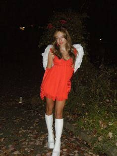 a woman in an orange dress and white boots is posing for the camera at night