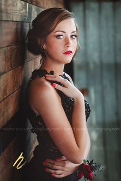 a woman in a black dress leaning against a wall with her hands on her chest