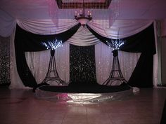 a stage set up for a party with black and white drapes, chandeliers and lights