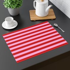 a red and white striped placemat next to a tea pot, coffee cup and spoon on a black table