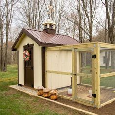 a small chicken coop in the middle of a field with trees and grass behind it