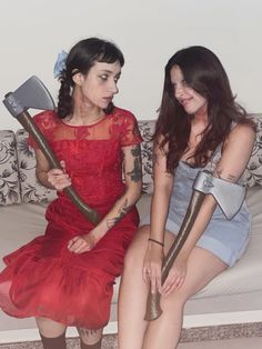 two women sitting on a couch holding axes and looking at each other's butts