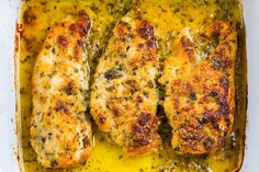 two pieces of chicken in a casserole dish with yellow sauce and herbs on top