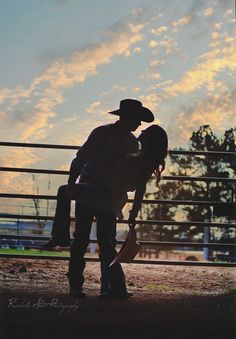 an image of two people kissing in front of a fence with the sun setting behind them