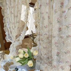 a table topped with plates and cups filled with food next to windows covered in curtains