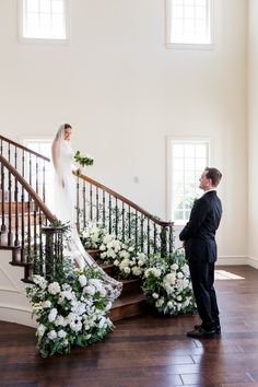 a bride and groom standing at the top of stairs in their wedding day attire with flowers