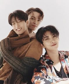 three young men sitting next to each other in front of a white background, one with his arm around the other's shoulder