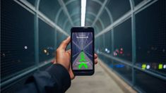 a person holding up a cell phone with a green arrow on it in a tunnel