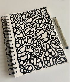 a notebook with black and white designs on it next to a marker, pen and paper