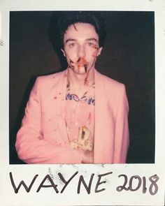 a man in a pink suit with blood all over his face and mouth, standing against a black background