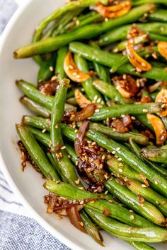 a white plate topped with green beans covered in sesame seeds