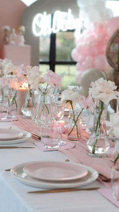 the table is set for a party with pink and white flowers in vases on it