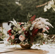 a vase filled with flowers sitting on top of a wooden table covered in greenery