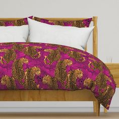 a bed with pink and brown comforter on top of it next to a wooden headboard