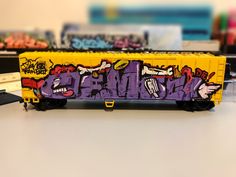 a yellow and purple train car with graffiti on it's side sitting on a table