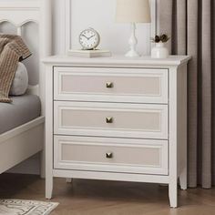 a white nightstand with two drawers and a clock on the night stand next to it