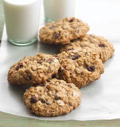 four oatmeal cookies and two glasses of milk on a napkin next to each other