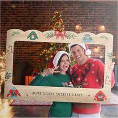 a man and woman holding up a wooden frame with an image of santa clause on it