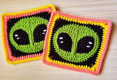 two crocheted coasters with faces on them sitting on top of a wooden table