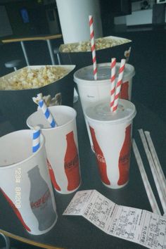 three cups with straws and two empty coke glasses on a table next to popcorn