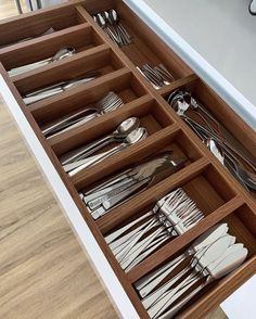 an open drawer with silverware in it on a wooden floor next to a counter