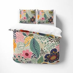 a bed with colorful flowers and leaves on the comforter, along with two pillows