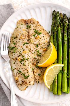 a white plate topped with fish and asparagus next to lemon wedges on a table