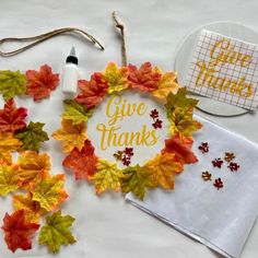 a white table topped with fall leaves and a paper plate filled with words that say give thanks