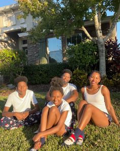 a group of kids sitting on the grass in front of a house with their arms around each other