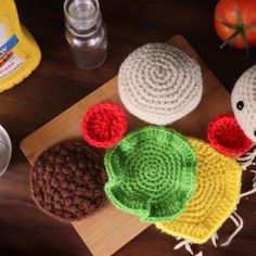 three crocheted hats sitting on top of a wooden cutting board next to tomatoes