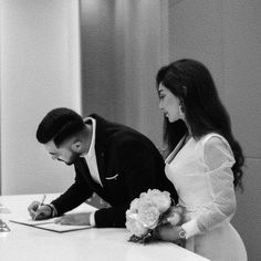 a bride and groom signing their wedding vows at the reception table in black and white