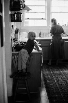 a little boy sitting on top of a chair in a kitchen next to a woman