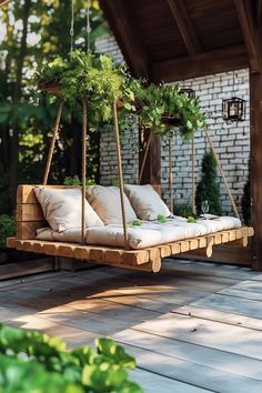 a wooden swing bed with pillows and plants on the back deck in front of a brick building