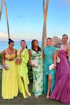 four beautiful women standing next to each other in front of palm trees and the ocean