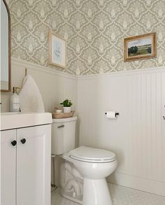 a white toilet sitting in a bathroom next to a sink and cabinet with pictures on the wall