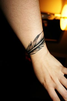 a person's hand with a feather tattoo on their left wrist, next to a lamp