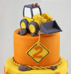 a yellow and orange birthday cake with a tractor on the top that says 2 in front of it