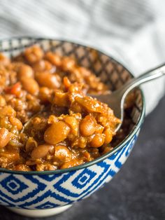 a blue and white bowl filled with beans on top of a black countertop next to a silver spoon