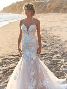 a woman standing on top of a beach next to the ocean wearing a wedding dress