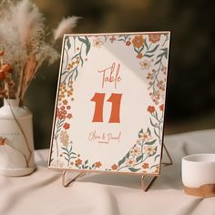 a table number sign sitting on top of a table next to a vase filled with flowers