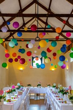 a room filled with tables covered in white table cloths and colorful balloons hanging from the ceiling