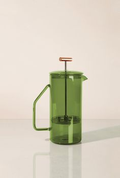 a green coffee pot with a wooden handle on a white surface, in front of a plain background