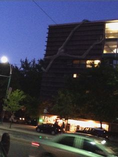 a car is driving down the street in front of a tall building at night time