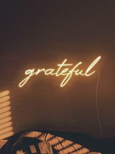 a neon sign that reads grateful on the wall next to a bed in a dark room