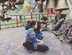 two people sitting on the ground in front of several bells hanging from it's sides