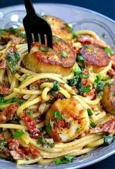 a fork is stuck into some pasta with scallops