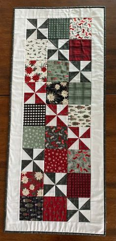 a quilted table runner with red and grey squares on it, sitting on a wooden floor